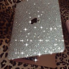 an apple laptop covered in silver sequins on a leopard print surface with a cell phone next to it