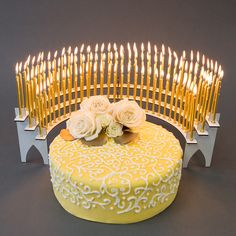 a yellow cake with white frosting and flowers on it next to a bunch of candles