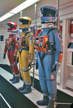 three mannequins dressed in space suits and helmets are lined up on a shelf