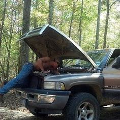 a man laying on the hood of a truck with his head in the open trunk