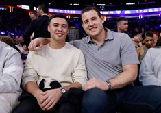 two men sitting next to each other in front of a crowd at a basketball game