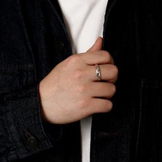 a person wearing a black jacket and white shirt with a silver ring on their finger