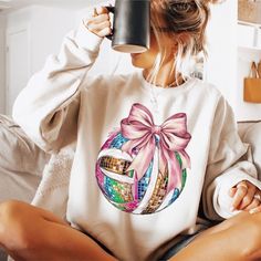 a woman sitting on a couch holding a coffee mug in her hand and wearing a sweater with a bow