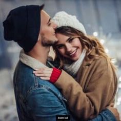 a man and woman embracing each other in front of a building with snow on the ground