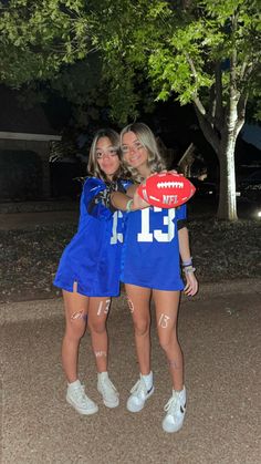 two girls in blue football uniforms posing for the camera with a red and white frisbee