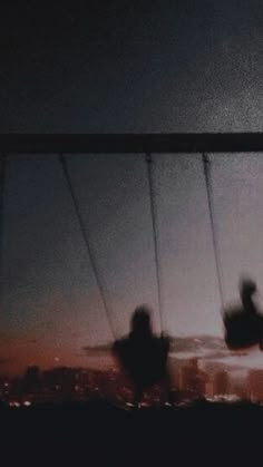 blurry photograph of two people on swings in the night sky with city lights behind them