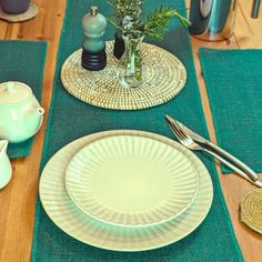 the table is set with plates, cups and teapots on green placemats