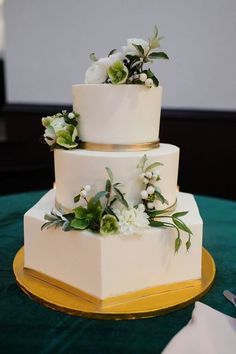 a three tiered wedding cake with white flowers and greenery