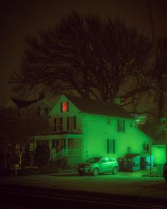 a green car parked in front of a white house on a dark street at night