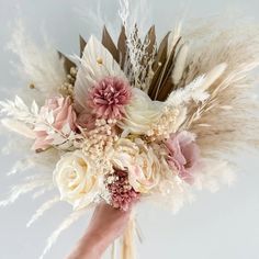 a bridal bouquet with feathers and flowers on it's head is held by a hand