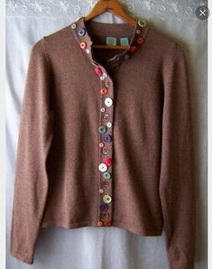 a brown sweater with buttons on it hanging from a hanger next to a white sheet