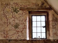 a window in an old stone building with vines painted on the wall and below it