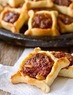 small pastries with meat in them sitting on top of napkins next to a pan