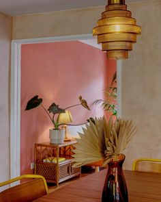 a vase with plants in it sitting on a wooden table next to a pink wall