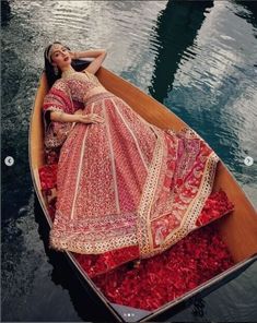 a woman in a red and white dress is sitting in a boat on the water