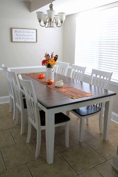 a dining room table with white chairs and flowers on the top one chair is empty