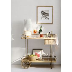 a gold bar cart with drinks on it in front of a white wall and framed photograph