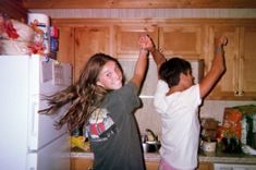 two young people standing in a kitchen with their arms up and one holding the other's hand