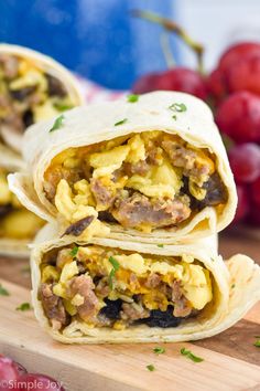 breakfast burritos are stacked on top of each other with grapes in the background