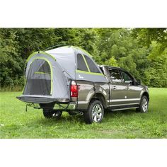 a truck with a tent attached to it's back in the grass next to trees