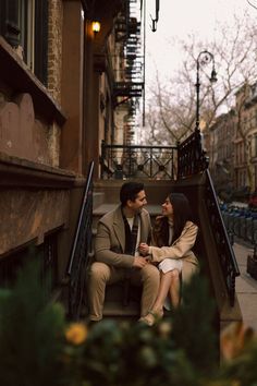 a man and woman sitting on steps in front of an apartment building, looking at each other