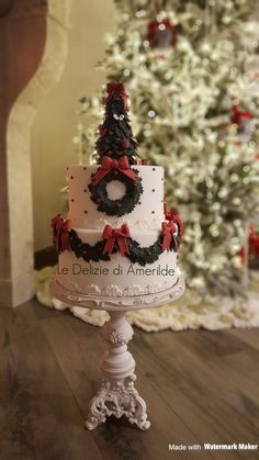 a three tiered cake decorated with wreaths and bows sits on a pedestal in front of a christmas tree