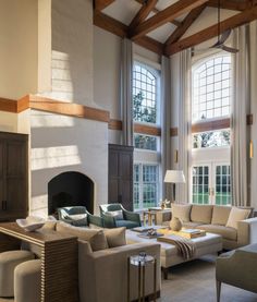 a living room filled with lots of furniture next to a fire place under two large windows