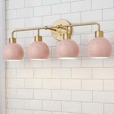 four light bathroom fixture with pink glass shades on white brick wall and gold metal bar