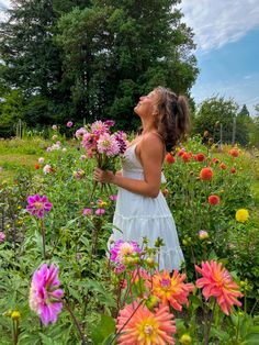 a woman standing in a field full of flowers holding a bunch of pink and yellow flowers