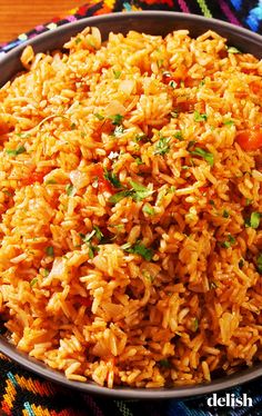 mexican rice with carrots and cilantro in a bowl on a colorful table cloth