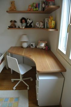 a white desk sitting under a window next to a shelf filled with stuffed animals and toys