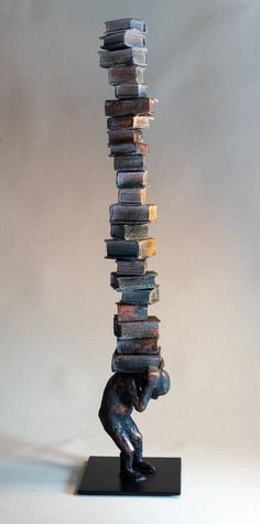 a sculpture of a man holding books on top of it's head with his hands in the air