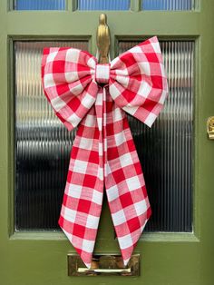 a red and white checkered bow hangs on the front door to a green door