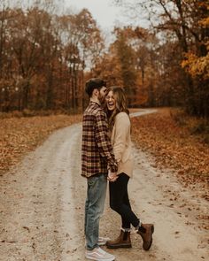 an engaged couple holding hands and walking down a dirt road in the fall with leaves on the ground