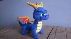 a crocheted blue and yellow dragon sitting on top of a wooden table next to a wall