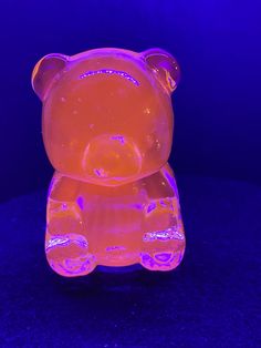 an illuminated teddy bear sitting on top of a blue surface in front of a purple background