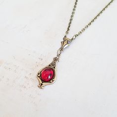 A classic and dainty art nouveau style antiqued brass pendant with a vintage ruby red Czech glass cabochon is suspended from an antique bronze chain. Choose your length in inches from the drop down menu. The pendant measures 1 1/2 inches (37 mm) from top to bottom, including the decorative connector. It is a quality USA made vintage style brass pendant with a lightly antiqued finish. The bright ruby red glass cabochon is vintage Czech glass. The antique bronze plated chain has a lobster clasp an Art Deco Jewelry With Antique Finish As Gift, Red Jewelry With Antique Finish As A Gift, Art Deco Antique Finish Jewelry Gift, Red Brass Necklaces As Gift, Red Antique Finish Jewelry As Gift, Red Brass Necklaces For Gift, Red Antique Finish Jewelry For Gift, Antique Gold Brass Necklace With Cabochon, Red Antique Finish Jewelry Gift