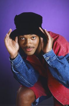 a young man wearing a denim jacket and hat with his hands on his head, posing for the camera