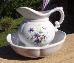 a white pitcher sitting on top of a wooden table next to a flag and flowers