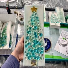 a person holding up a christmas tree made out of glass beads and other crafting supplies