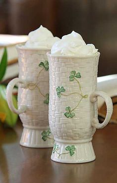 two mugs with whipped cream on them sitting on a table