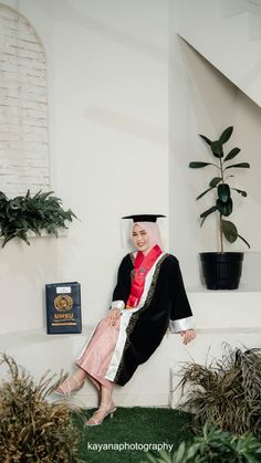 a woman in a graduation gown sitting on a ledge next to some potted plants