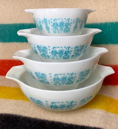 three white and blue bowls stacked on top of each other in front of a striped background