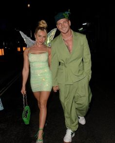 a man and woman dressed up in costumes walking down the street at night with fairy wings on their head