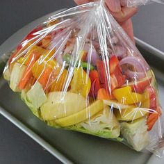 a person is holding a plastic bag full of fresh fruit and veggie salad