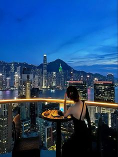 a woman sitting at a table on top of a tall building with a view of the city