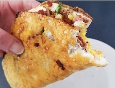 a hand holding up a piece of food on top of a white sauce covered plate