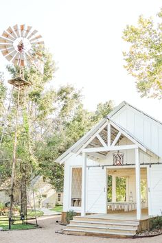 a small white house with a windmill in the back ground and trees around it,