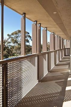 an empty balcony with lots of perfored screens on the wall and trees in the background