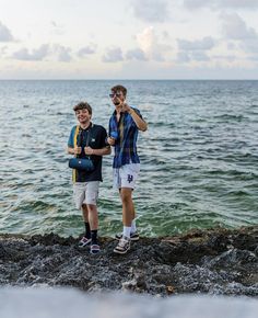 two young men standing on rocks near the ocean